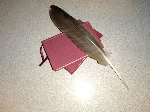 A reference to Shakespeare with two red leatherbound notebooks and a quill
  